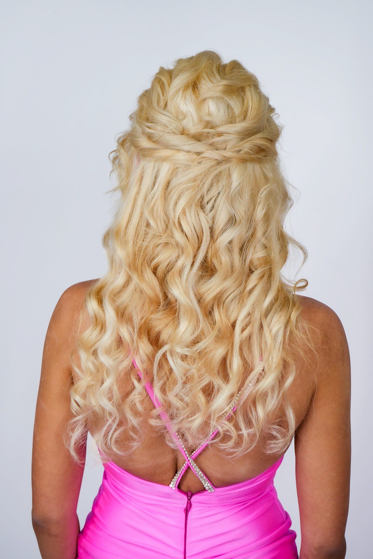 Woman with long blonde hair styled in curly half up half down hairstyle, voluminous waves for wedding or formal event look.